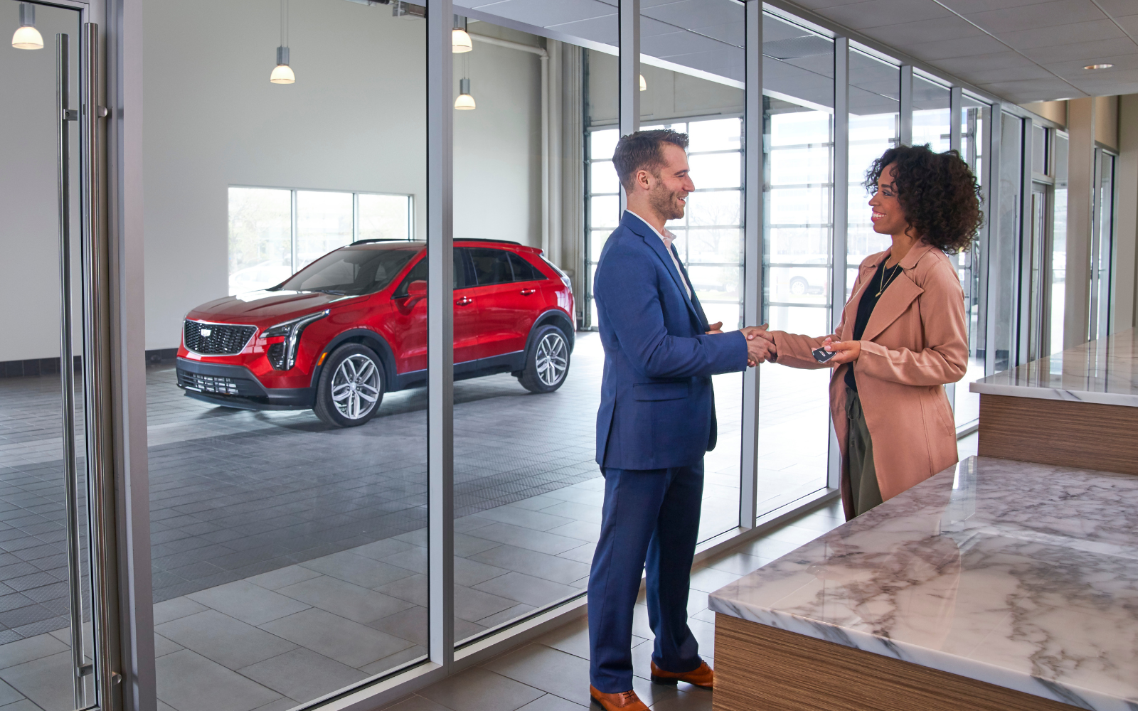 Man shaking hands with a woman in front of new Cadillac vehicle
